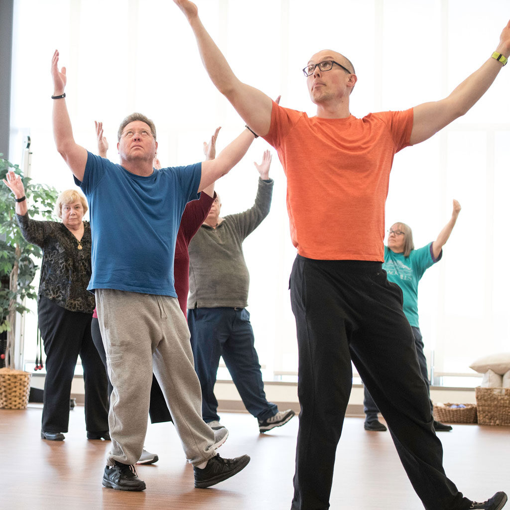 Participants in a Tai Ji Quan class with arms raised