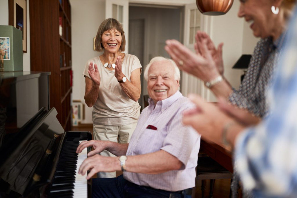 Photo of a group of people listening to an older adult play the piano.