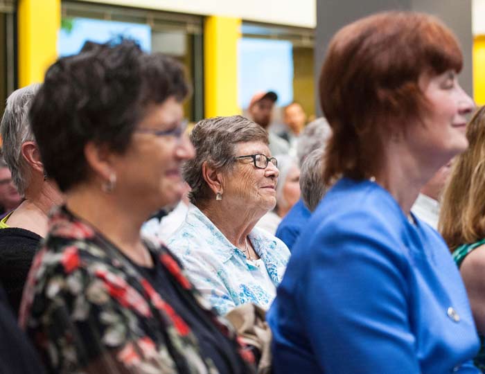older woman in a crowd, listening intently.