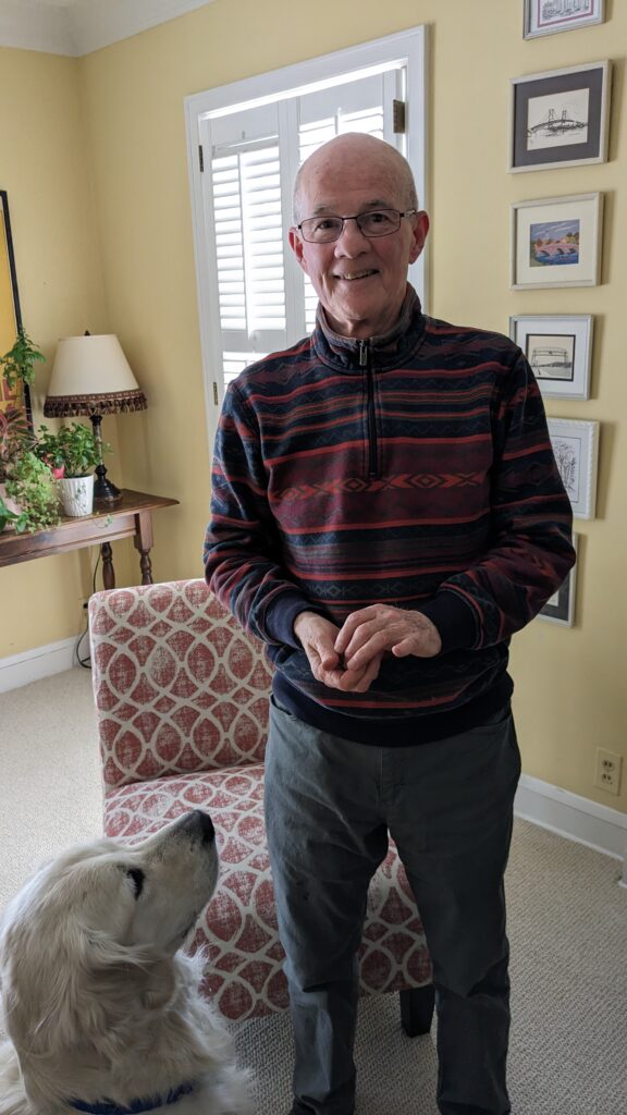 Bob Besinger posing for a photo. His dog, Odin is looking up at him.
