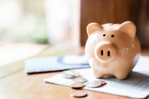 A piggy bank on a wooden table next to a few coins.