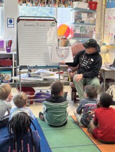 Photo of a person reading to a classroom seated on the floor.