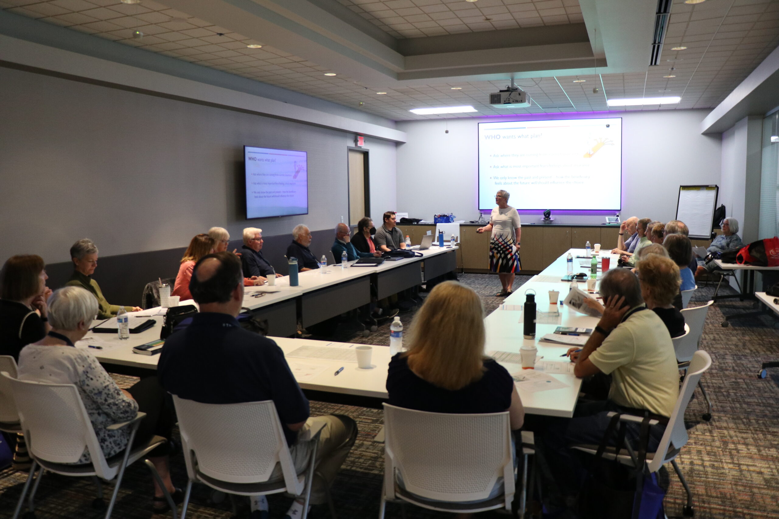 Attendees sitting at U-shaped table watching presentation.