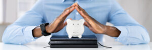 Close up photo of hands covering a piggy bank.