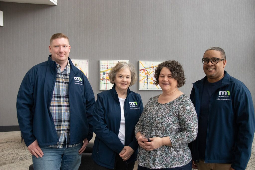 Four presentation team members dressed in logo jackets smiling at camera.