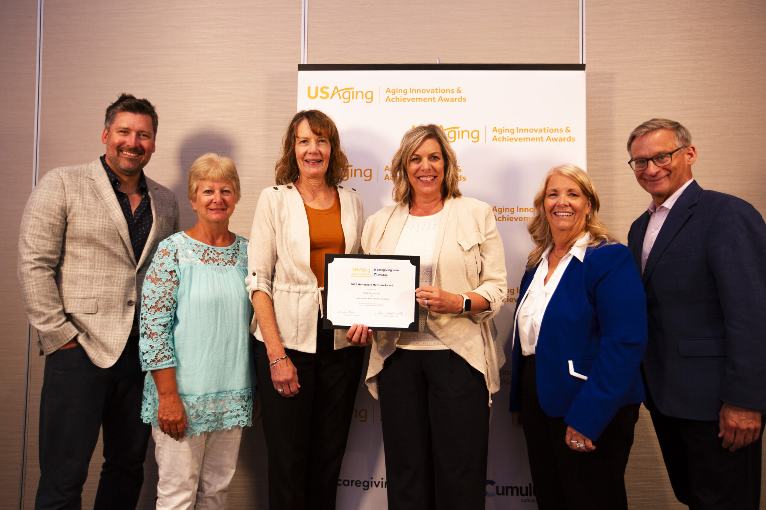 Six people standing in front of a USAging banner. The woman in the middle is holding a certificate.