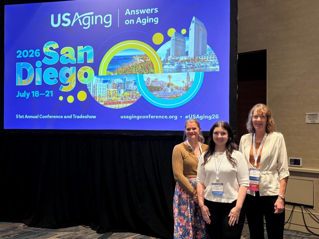 Three women standing in front of a projected screen advertising the 2026 USAging Conference.