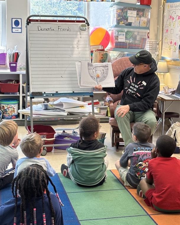 A man reading a book to a classroom of young children seated on the floor.